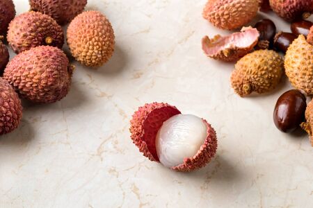 Whole lychee, shells and bones near half peeled lychee fruit (Litchi chinensis) on a white kithen table. Fruits and vegetables, vegetarian and healthy eating. Front view.の写真素材