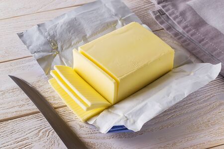 Slices of fresh yellow butter cut off from a just opened pack and knife on a white wooden table. Dairy. Sandwich butter. Natural fat nutrient. Front view. の写真素材