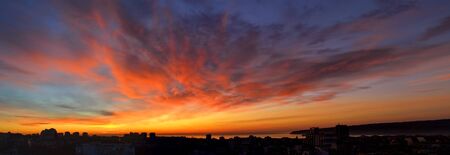 Panorama of dawn fire in the sky over a small seaside city. Golden red clouds just before the sunrise. Scenic landscape at sunrise. Beauty in nature.の写真素材
