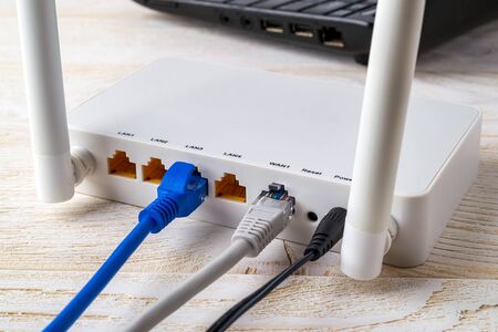 Close-up of network cables connected to a white WiFi wireless router near laptop on a white wooden...