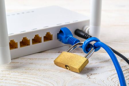 White WiFi wireless router with padlock on a blue network cable on a white wooden  table. Forbidden...