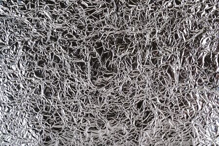 Creased aluminum foil texture. Sheet of crumpled silver foil with shiny folds for background. Metal wrinkled surface as graphic resource. Top view.の写真素材