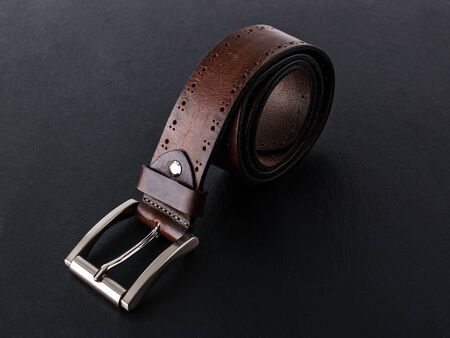 Brown belt made of genuine leather with classic metal buckle on a black surface. Men's stylish...