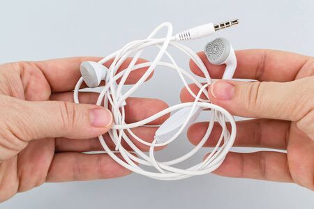 Female hands holding tangled earphones on a gray background. White tangled headphones. Modern personal device for music and communication. Front view. の写真素材