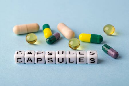 Word Capsules made of white cubes and different capsules on a blue medical background. To get sick, take pills or undergo treatment concept. Health care. Front view.の写真素材