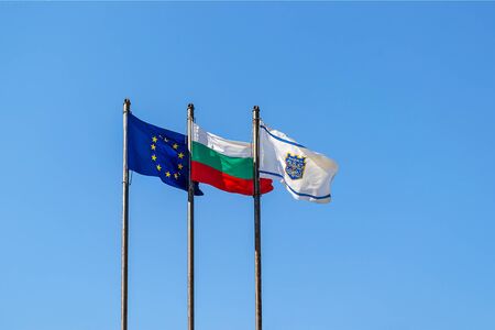 Three flags on a poles against bright blue sky: EU, Bulgaria and with the coat of arms of Varna city...