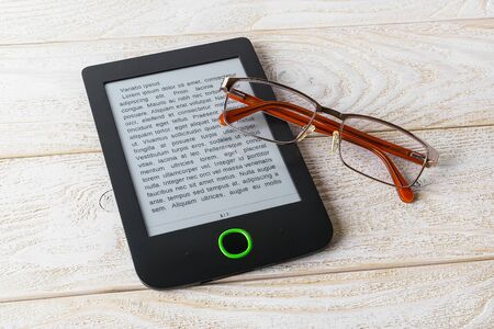 Vision glasses on e-book over a white wooden table. Digital tablet device with anti-glare screen....