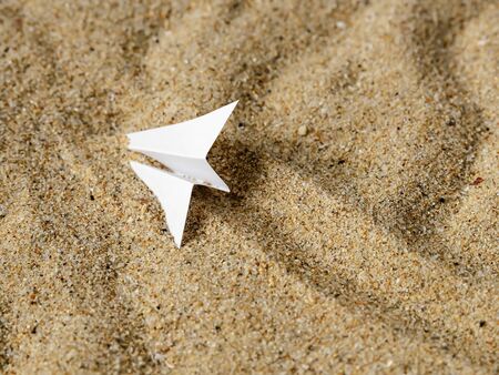 White paper plane on a yellow wavy sand. Metaphor of a plane crash, hard landing outside an aerodrome, air accident. Top view.の写真素材