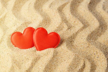 Two red silk hearts on a yellow wavy sea sand. Concept of love, sun, hot summer, sea holiday and vacation on a beach. Top view.の写真素材