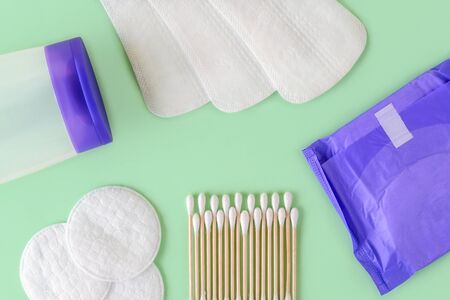 Feminine hygiene items: panty liners, regular sanitary pad, cotton pads, cotton buds wood stick and cleansing lotion on a pastel mint background. Flat lay. Top view.の写真素材