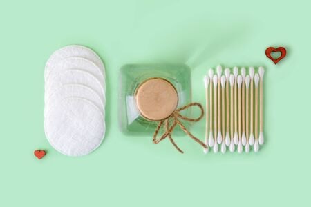 Cleansing lotion or tonic in a glass jar, cotton pads and cotton buds wood stick on a pastel mint...