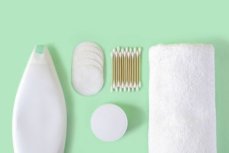 Shampoo, cotton pads, cotton buds wood stick, face cream and white terry towel on a pastel mint...