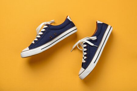 Pair of classic blue sneakers or gumshoes with white shoe laces on a textured yellow background....