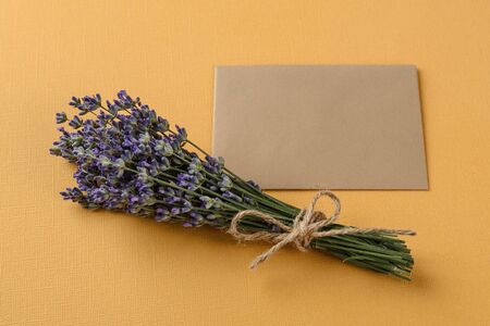 Small bouquet of fragrant blooming lavender near a blank sheet of brown paper for notes over a textural yellow background. Summer and romantic greeting card with copy space. Top view.の写真素材