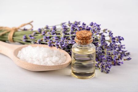 Lavender essential oil, cosmetic bath salt in a wood spoon and fresh fragrant lavender on a white wood surface. Home made spa, skincare and cosmetology concept. Front view.の写真素材