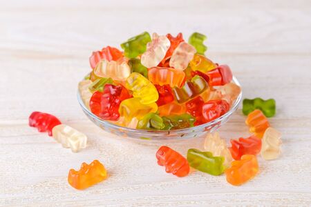 Multicolored gummy bears candy on a glass plate over white wood table. Jelly sweets of differenr colors. Popular gummies made from fruit juice, gelatin and sugar. Front view.の写真素材
