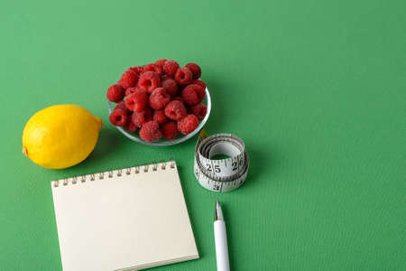 Inch measuring tape roll, lemon, raspberries, paper notepad and white pen on a green background. Concept of healthy eating, diet, weight loss and body slim. Copy space.の写真素材