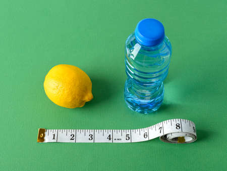 Inch measuring tape, ripe lemon and bottle of pure drinking water on a green background. Concept of healthy eating, diet, weight loss and body slim. Top view.の写真素材
