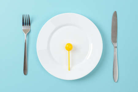 Yellow sweet caramel candy on a white dinner plate, table knife and fork on a blue background. Concept of unhealthy eating with excess carbohydrates. Top view.の写真素材