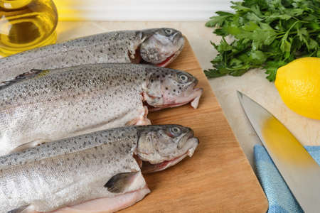 Close-up of three raw gutted trout fishes on a wood cutting board prepared for cooking. Fresh fish dishes, healthy eating and cook at home concept. Top view.の写真素材