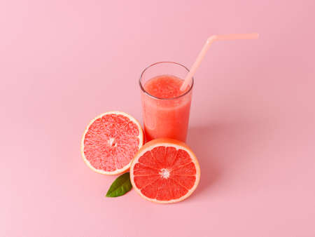 Glass of freshly squeezed grapefruit juice with pulp, drinking straw and two halves of grapefruit on a pink background. Vegetarian, raw food diet and healthy eating. Top view.の写真素材