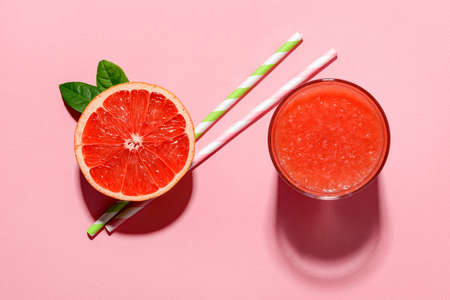 Glass of freshly squeezed grapefruit juice with pulp, half grapefruit and two drinking straws  cast shadows in bright light on a pink background. Vegetarian, raw food diet and healthy eating. Top view.の写真素材