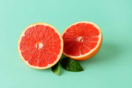 Two halves of fresh ripe juicy grapefruit and two leaves on a mint green background. Vegetarian, raw food diet and healthy eating. Organic antioxidant. Front view.の写真素材