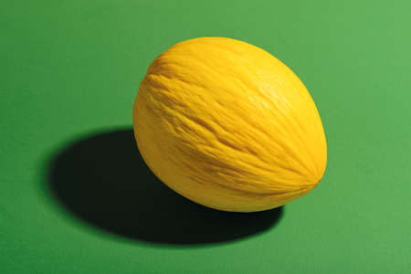Whole ripe honeydew melon with yellow peel on a textured green background. Shot with hard light. Sweet fruits and berries. Vegetarian, raw food diet and healthy eating. Front view.の写真素材
