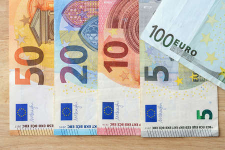 Banknotes of 5, 10, 20, 50, 100 euro on a brown wooden table. Euro paper currency of different face...