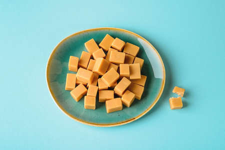 Pile of caramel vanilla fudge on a turquoise ceramic plate over turquoise background. Fresh tasty candies made of milk and sugar. Square pieces of delicious soft sweets. Top view.の写真素材