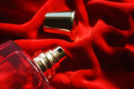 Glass bottle of fragrant perfume or scented toilet water with a golden cap on folded scarlet velvet. Love and passion concept. Top view.の写真素材