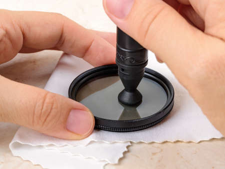 Hands polish a camera polarizing filter using lens pen soft felt end over microfiber cloth. Routine removal of dust and fingerprints from photographic equipment. Maintenance close-up. Front view.の写真素材