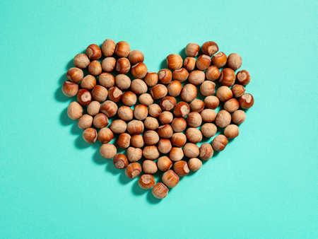 Heart shape made of unpeeled hazelnuts casts shadows on a turquoise paper background. Nuts as an antioxidant and protein source for ketogenic diet and vegetarianism. Top view.の写真素材