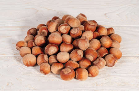 Pile of unpeeled hazelnuts over white wood table. Nuts as an antioxidant and protein source for...