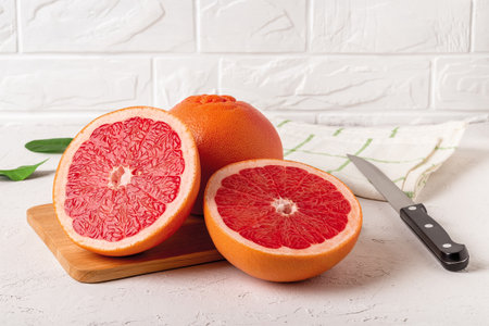 Whole ripe grapefruit and two juicy halves on a cutting board and knife. Ingredient for fruit desserts. Tasty vegetarian food, slimming diet and vitamin healthy eating. Top view.の写真素材