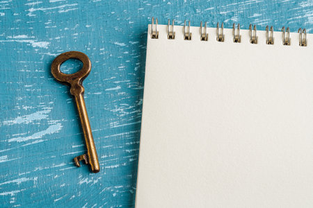 Brown metal shabby vintage key near spring notepad on a turquoise scratched paint surface. Leave or receive a note and a key. Copy space. Top view.の写真素材