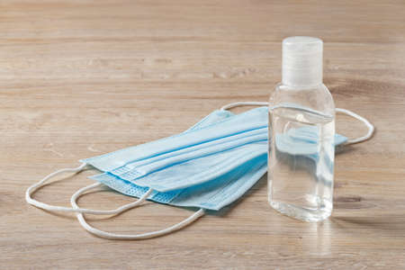 Two disposable medical face masks and disinfecting hand sanitizer in a small bottle on a brown desk. Personal protection against viral infections,   flu. Health care. Front view.の写真素材