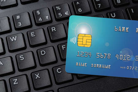 Closeup of blue credit card on the black computer keyboard. Online shopping and payments, making orders via Internet, electronic banking concepts. Top view.の写真素材