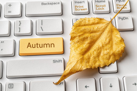 Yellow key with Autumn word and fallen leaf on a white computer keyboard. Autumn sales, holidays, school and working season concepts. Keypad enter button with message. Top view.の写真素材
