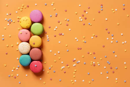 Set of multicolored macaroons on an orange background with small stars. Mockup of greeting card with sweet multicolored macaron cakes. Delicious french almond meringue cookies. Copy space. Top view.の写真素材