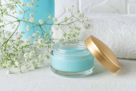 Open jar of blue moisturizing facial gel near white terry towel in a bathroom. Hydrating face cream in a glass container with golden lid. Beauty, skincare and cosmetology concept. Health care. Close-up.の写真素材
