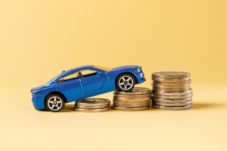 Blue toy car rides up a stack of coins against yellow background. Concepts of costs of car insurance, buying, service, repair and renting. Car investment. Saving money for a car. Front view.の写真素材