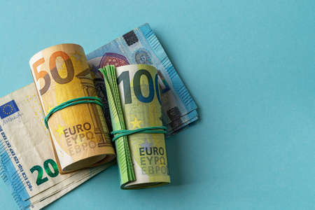 Green roll of 100 euro banknotes and orange roll of 50 euro bills over 20 euro paper money against...