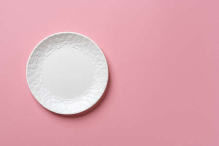 White round ceramic plate with checkered ornament on the edge over textured pastel pink background. Modern empty dishes and crockery for stylish food design. Copy space. Top view.の写真素材
