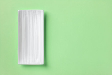 White rectangular ceramic plate over mint green textured background. Empty flat plate with grooved...