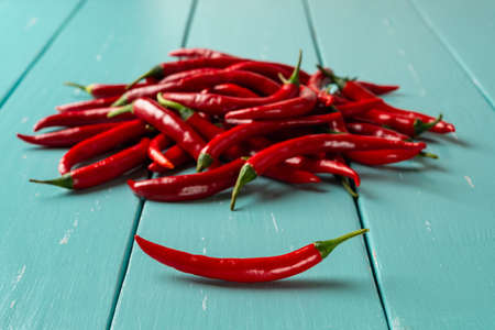 Red hot chili pepper pod in front of raw chilli peppers pile over turquoise wooden table. Whole fresh pungent chiles for cooking. Spicy dishes organic ingredient. Focus on the foreground. Close-up.の写真素材
