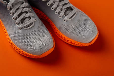 Pair of grooved orange sole sneakers from gray mesh fabric over orange background. Laced up stylish ...