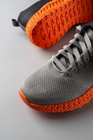 Grooved orange sole sneakers with gray elastic laces over grey background. Pair of new mesh fabric...