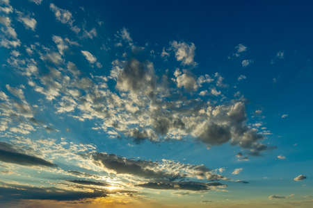Yellow rays of the setting sun shine in a cloud gap low above the horizon and illuminate a...