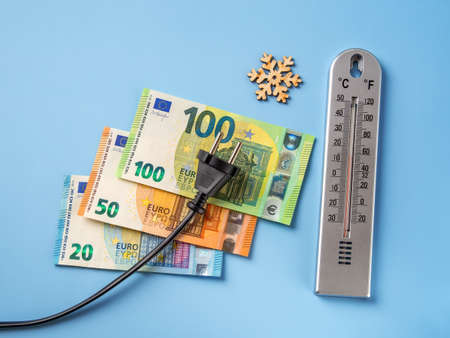 Black electric plug over 20, 50 and 100 euro banknotes, snowflake and air thermometer over blue background. Rise in electricity prices in the cold winter season, increasing cost of electricity concept.の写真素材